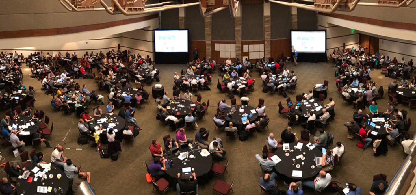 Large room with several round tables full of people doing scaled agile training